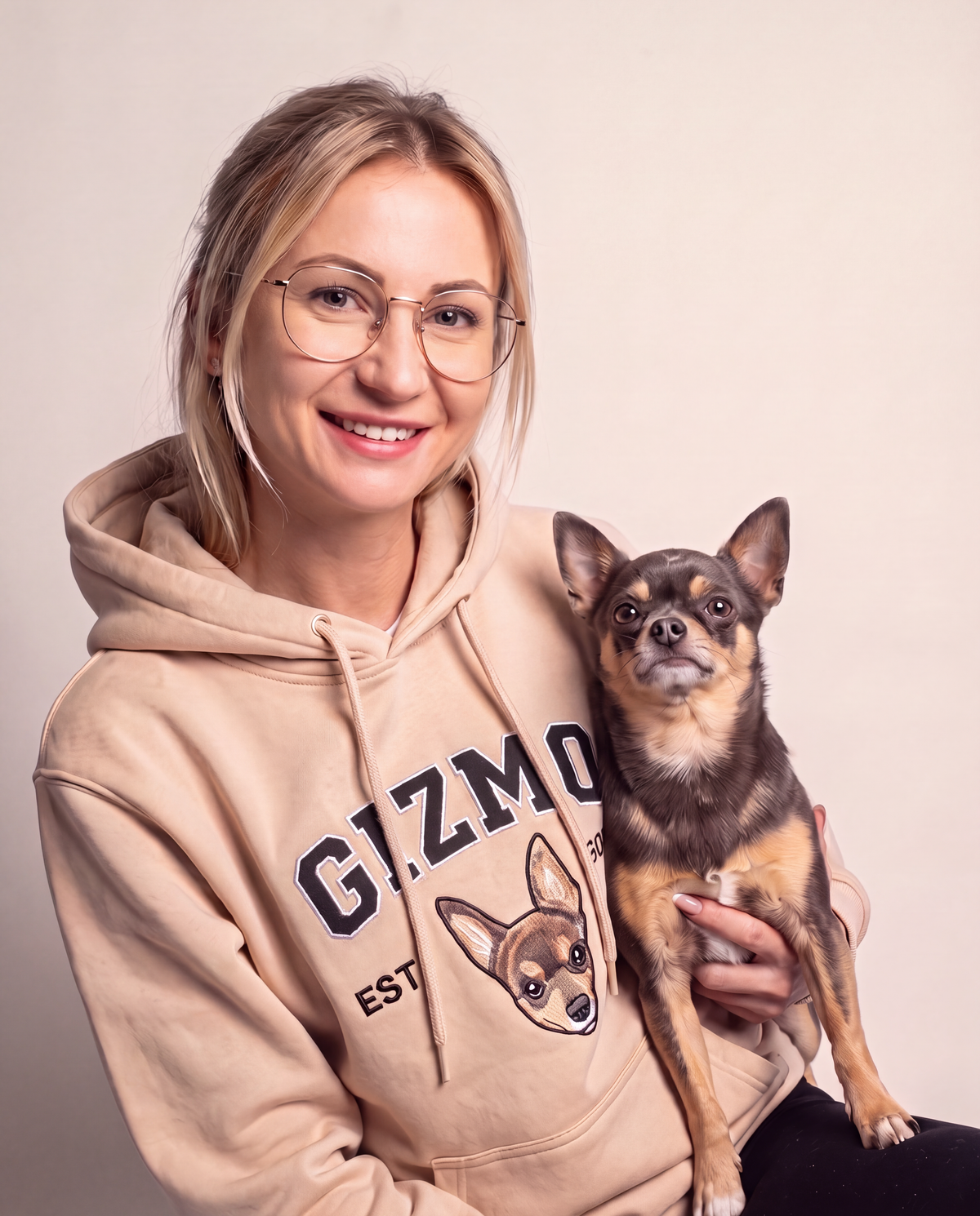 Customer in a beige University hoodie holding the chihuahua embroidered on it